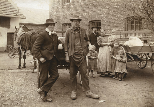 Im Vordergrund zwei Bauern mit Pferdefuhrwerk und hinten 1. Generation Dorfner mit vier Kindern